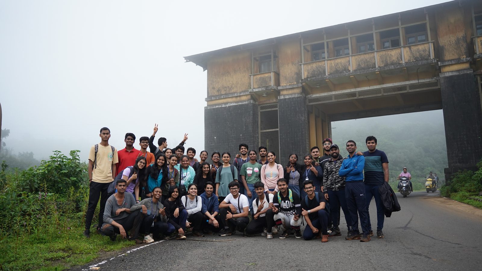 A large Lavasa Trekkers group on a misty road beneath an old gateway building